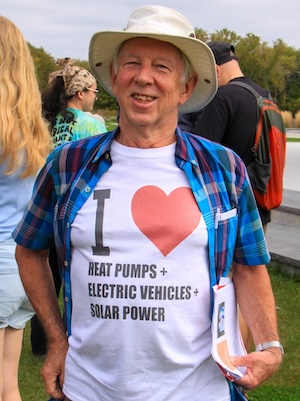 A smiling older man in a sun hat wears a T-shirt that reads: I love heat pumps, electric vehicles and solar power.