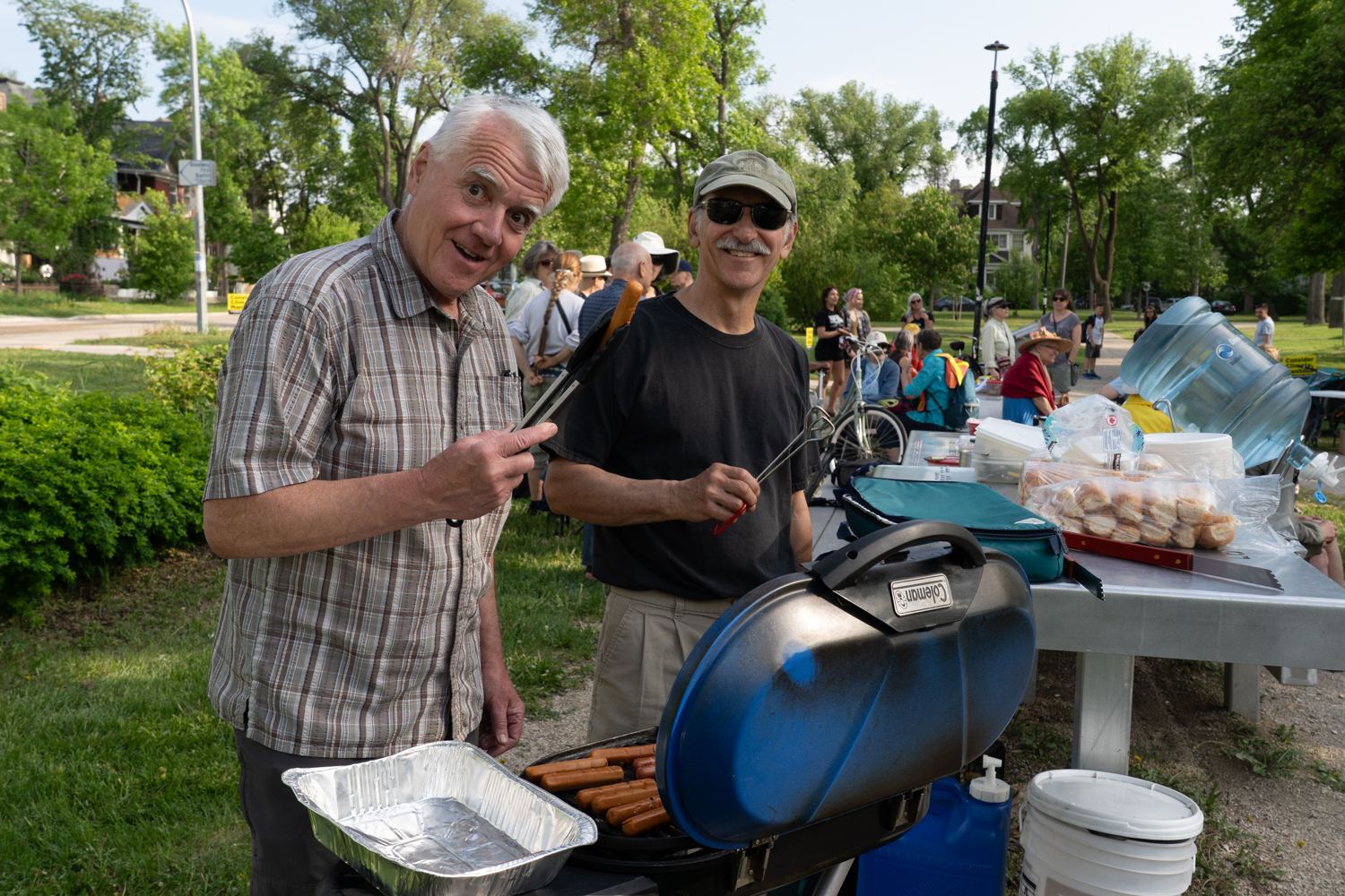 Deux hommes âgés sourient lors d’un barbecue de groupe dans un parc.