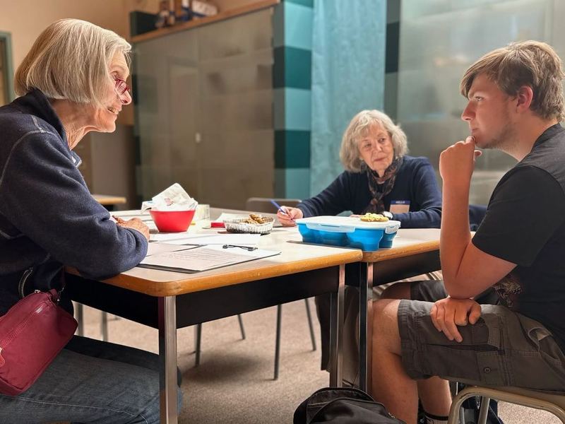 Deux femmes âgées discutent avec un jeune homme autour d’une table, lors d’un café climat.