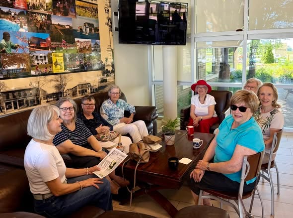Des aînés discutent sur des canapés et des fauteuils autour d’une table basse, dans un café.