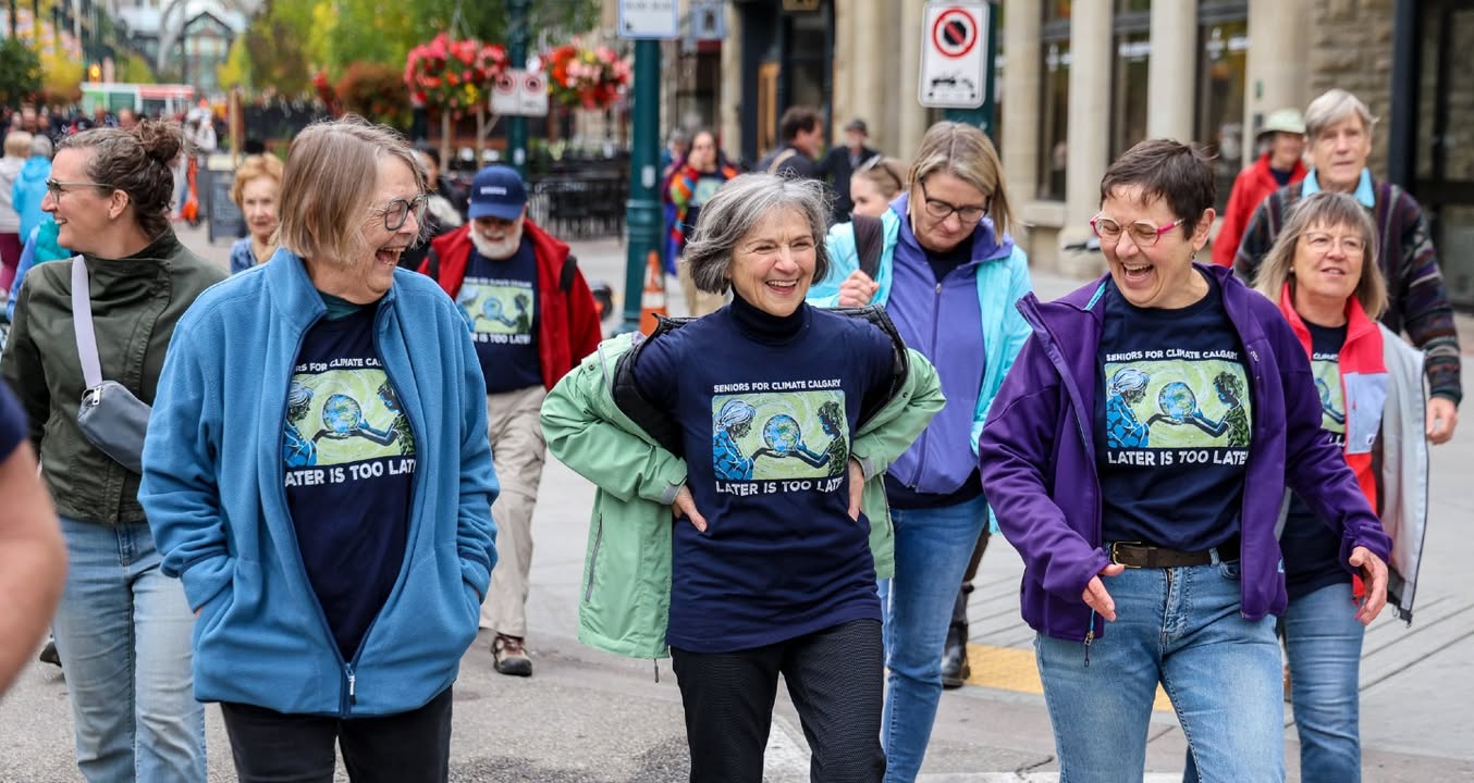 Laughing seniors in matching Seniors for Climate T-shirts walk together down a downtown street.