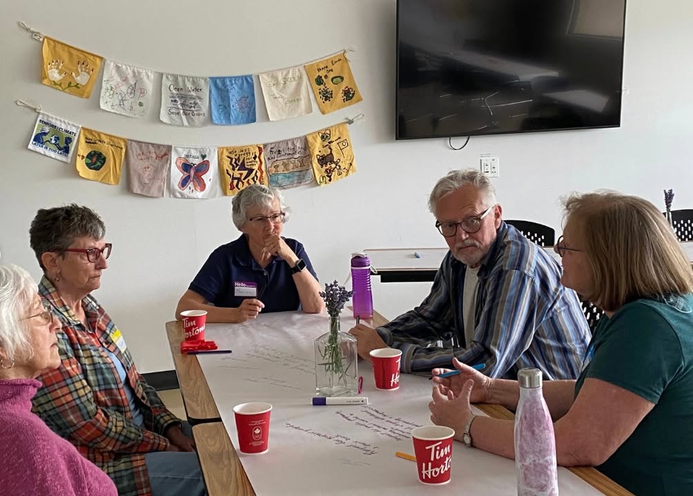Five seniors talk around a table, under a line of hand-painted cloth flags.