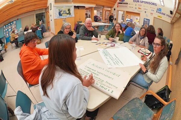 Des aînés, réunis autour de tables dans un centre communautaire, dressent une liste d’actions sur de grandes feuilles.
